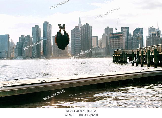 USA, New York, Brooklyn, young men doing backflip on pier in front of Manhattan skyline