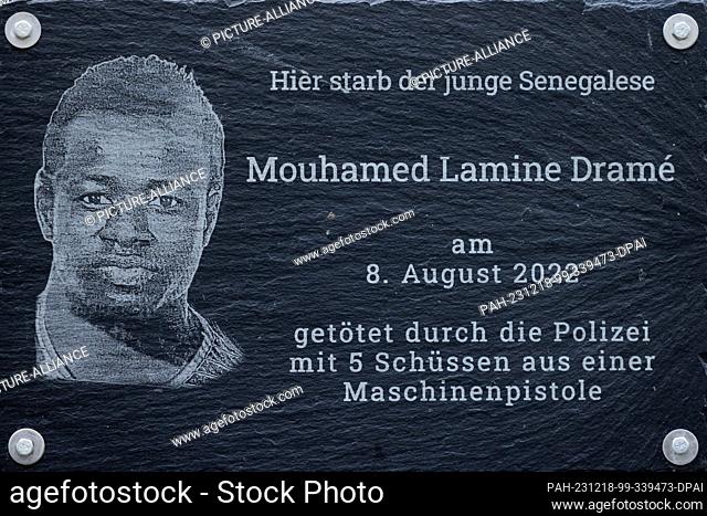 PRODUCTION - 18 December 2023, North Rhine-Westphalia, Dortmund: Posters and a plaque at the crime scene (behind the fence) commemorate 16-year-old Senegalese...