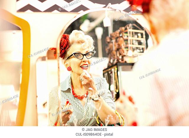 Mirror image of quirky vintage woman applying lipstick in antique and vintage emporium