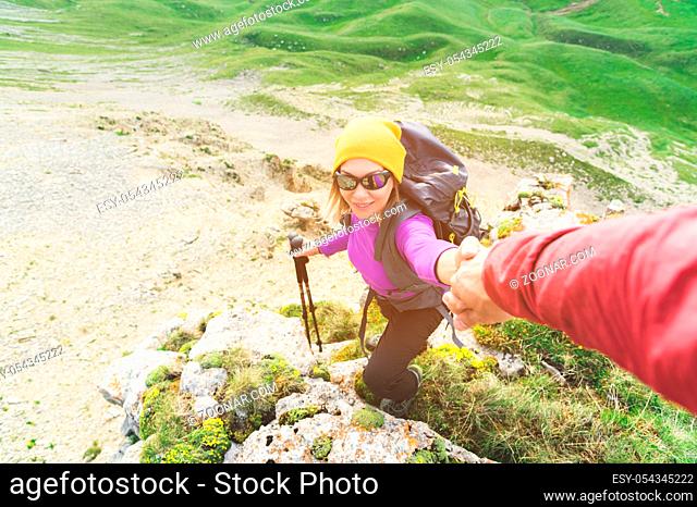 A climber helps a young mountaineer woman reach the top of the mountain. A man gives a helping hand to a woman. View from above