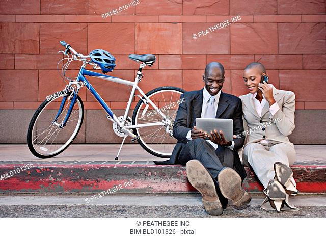 Business people sitting on curb using digital tablet and cell phone