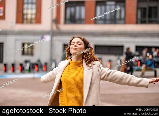 Carefree young woman with arms outstretched standing on footpath
