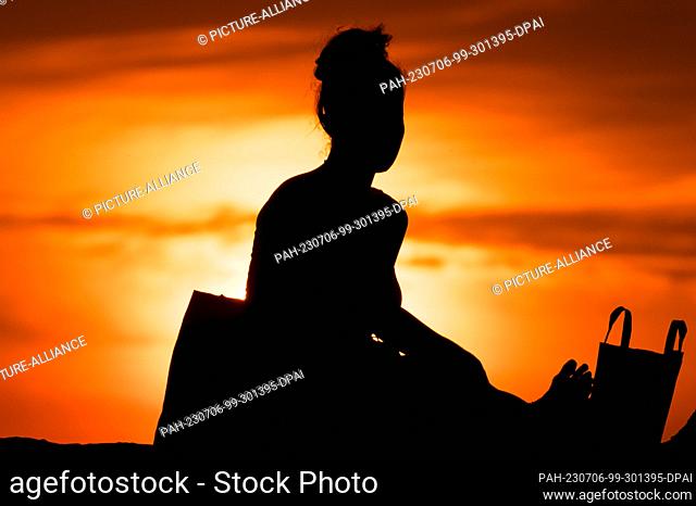 SYMBOL - 05 July 2023, Serbia, Belgrad: A woman sits on a wall at Kalemegdan Park at sunset. Thereby she can be seen as a silhouette