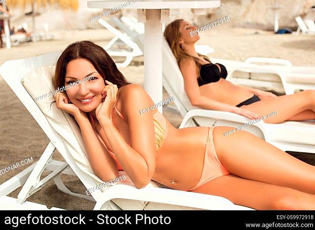 Two beautiful young women lying on sunbeds on sandy public beach. Outdoor shot. Tenerife