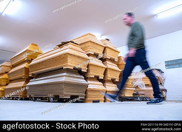 12 November 2020, Lower Saxony, Glandorf: Udo Mentrup, managing director of the coffin manufacturer Schmidt-Hendker, passes several stacked coffins in a...