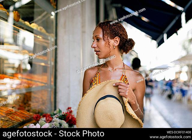 Hungry young woman with hat looking through delicatessen store window