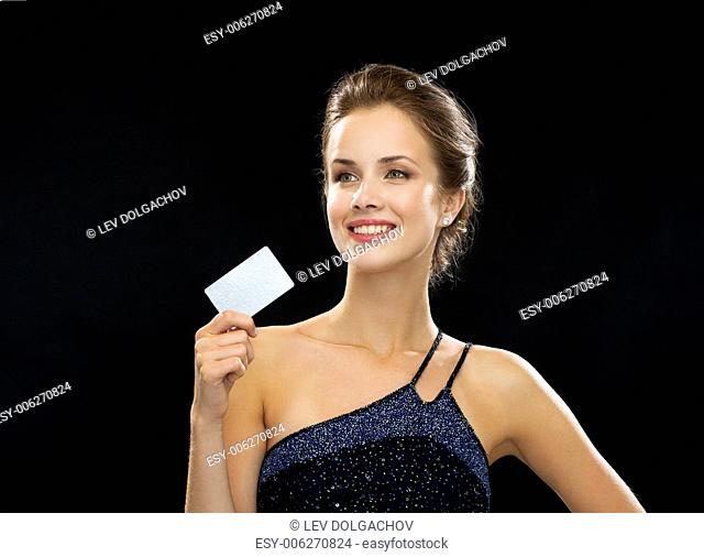 wealth, money, luxury and people concept - smiling woman in evening dress holding credit card over black background