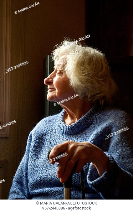 Portrait of old woman at home, smiling and looking at the window. Low key