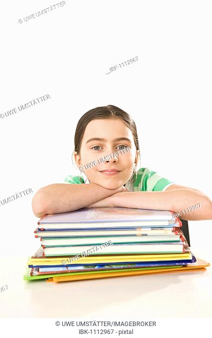 Smiling girl sitting in front of a pile of exercise books and school books