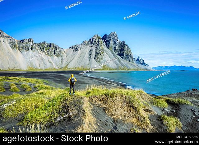 man with backpack on black sand dune on the stokksnes headland on southeastern icelandic coast with vestrahorn summer panorama of iceland, europe