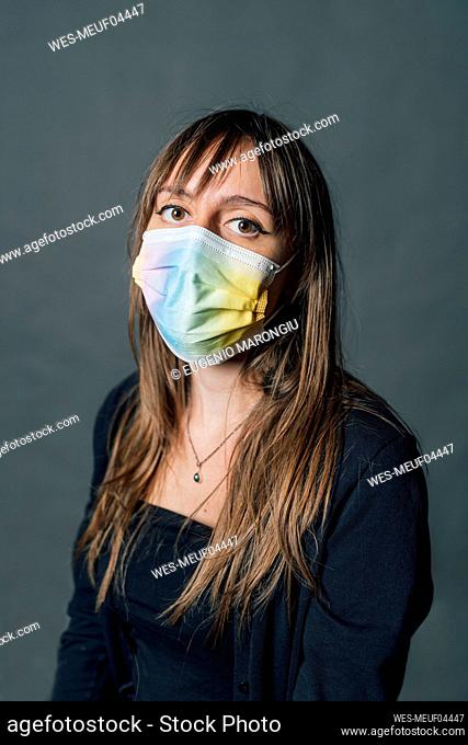 Young woman wearing multi colored protective face mask against gray background