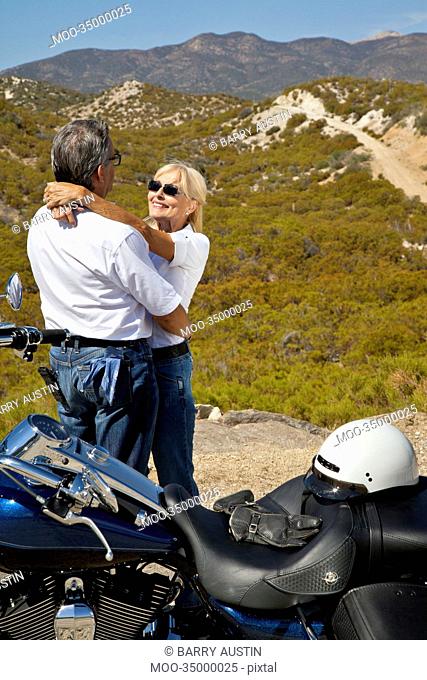 Senior couple embrace next to motorcycle in the desert