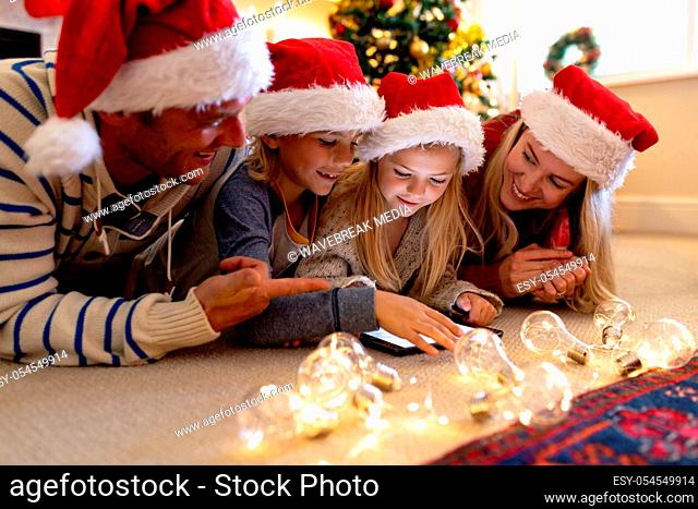 Front view of a Caucasian couple lying on the floor with their young son and daughter in their sitting room at Christmas time