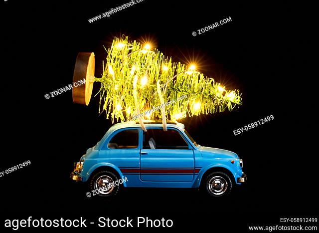 Blue retro toy car delivering Christmas or New Year illuminated tree on black background