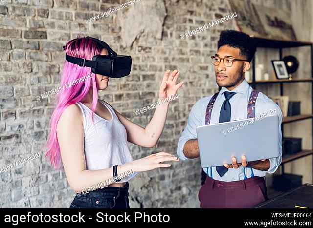 Two creative business people with VR goggles and laptop in loft office