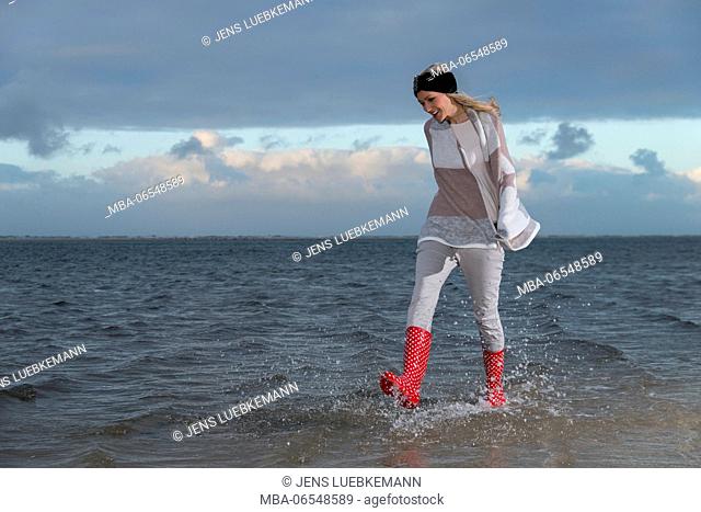 Woman with red boots running through the water at the sea