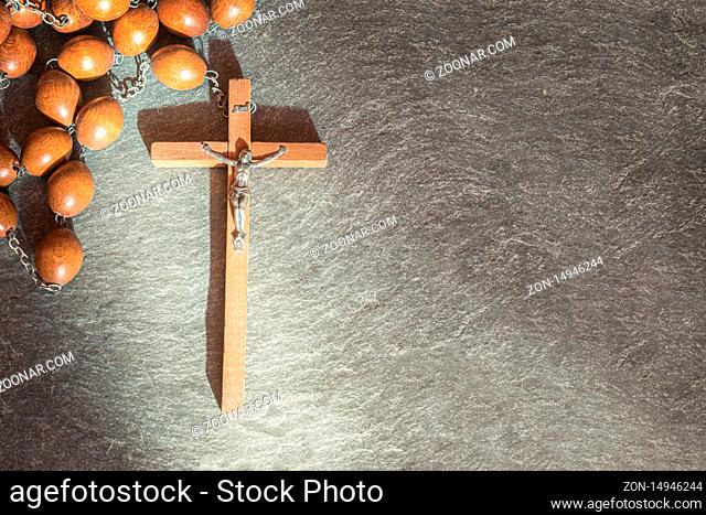 Old wooden Franciscan rosary, on the large Christian cross Jesus, a ray of sunshine illuminates the rosary on a gray stone background