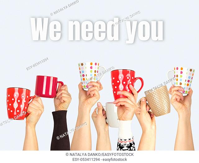 many hands raised up and holding ceramic cups on a gray background, inscription we need you, concept of recruitment in the company