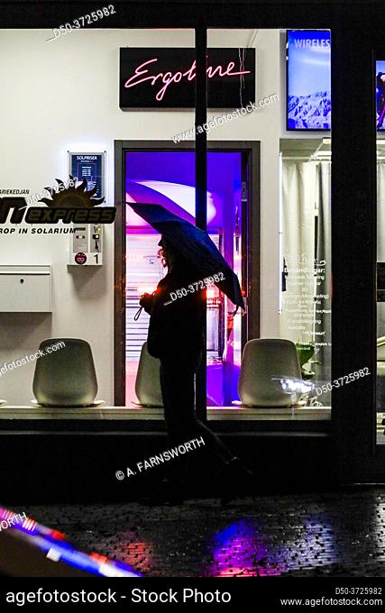 Stockholm, Sweden A woman with an umbrella walks by a tanning salon in Liljeholmen at night