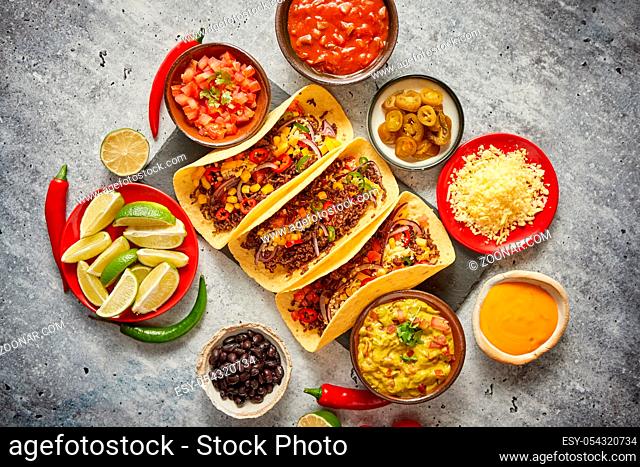 Tasty Mexican meat tacos served with various vegetables and salsa. With sides in ceramic bowls around. Top view composition