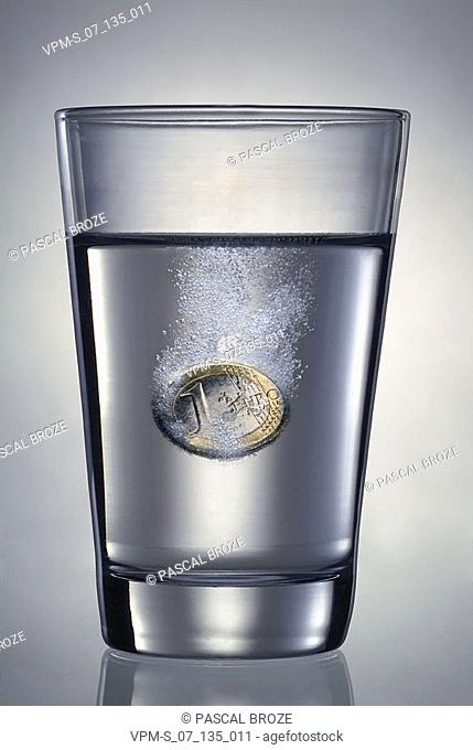 Close-up of one Euro coin dissolving in a glass of water