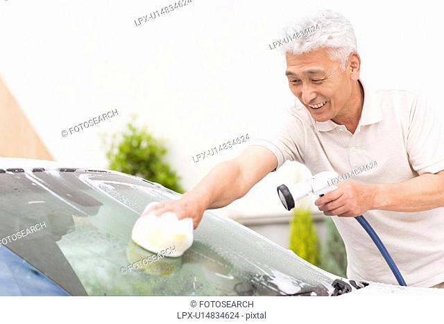 Senior man washing car, holding hose and sponge