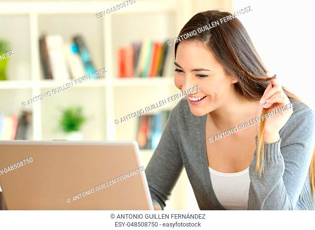 Candid girl dating on line with a laptop and touching hair sitting at home