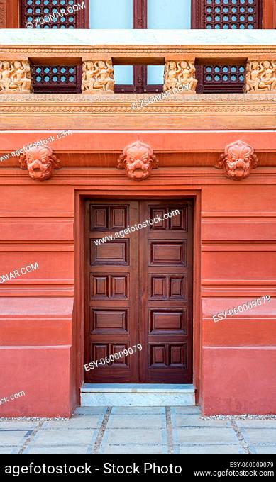 Recessed engraved closed wooden door installed in ornamental stone wall outside of old building with decorated balustrade above
