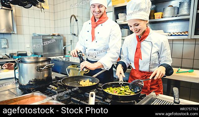 Team of chefs in a kitchen preparing fantastic food in pans, man and woman