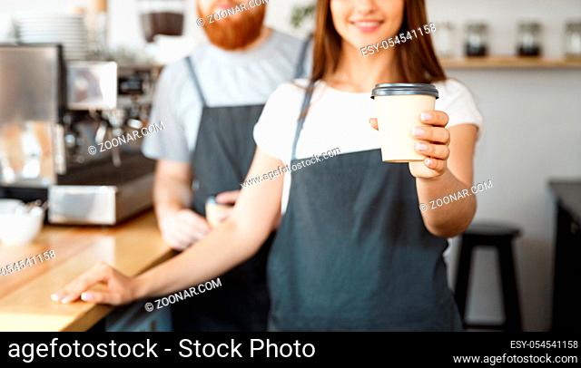 Coffee Business Concept - Positive young bearded man and beautiful attractive lady barista couple giving take away cup of coffee to custome at the modern coffee...
