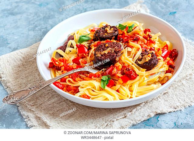 Fork in a plate with Italian pasta, tomato sauce, red pepper and blood sausages