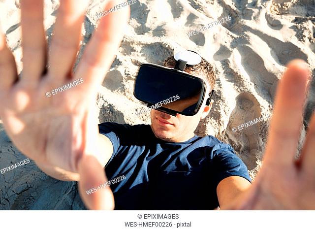 Man wearing VR glasses lying in sand on the beach