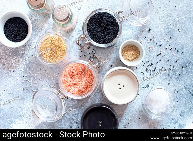 Mix of different salt types on grey concrete background. Sea salts, black and pink Himalayan salt crystals, powder. collection of different types of salt