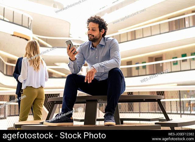 Smiling businessman using smart phone with colleagues in background at corridor