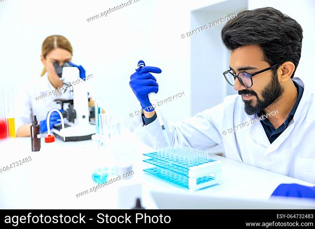 Team of scientists examining sample, female doctor using microscope, male researcher working with chemical liquids in flask in modern lab