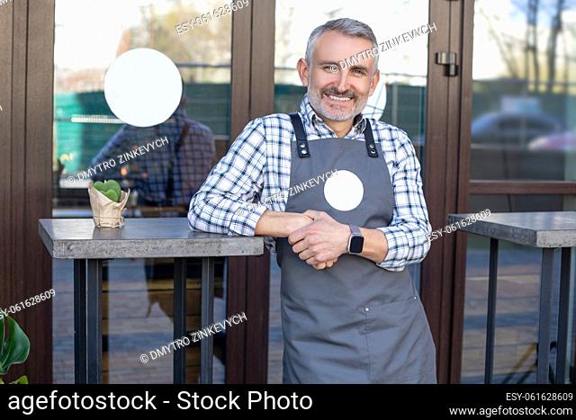 Good day. Cafe owner standing near the table outside and looking happy