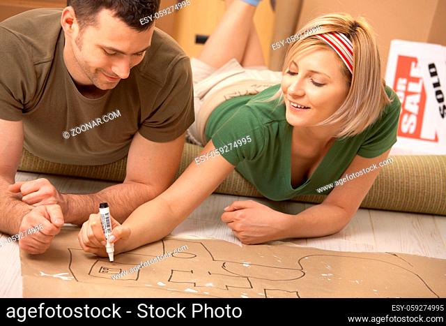 Happy couple planning to furniture the new house after moving in, girl drawing with marker on paper