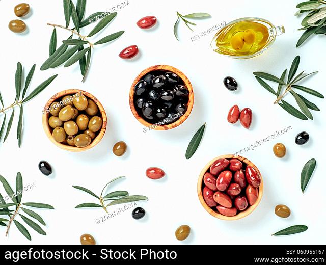 Set of green olives, black olives and red kalmata olives and extra virgin olive oil on white background. Top view of different types of olives in bowls and oil...
