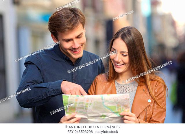 Front view portrait of a happy couple of tourists on vacation using a paper map in the street