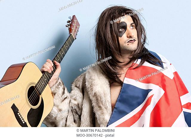 Young man with British flag holding guitar against light blue background
