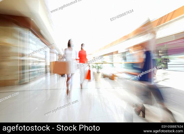 Abstract defocused motion blur background of girls walking fast in shopping mall with bags