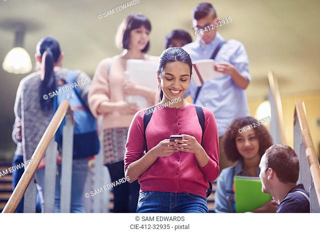 Smiling female college student texting in stairway