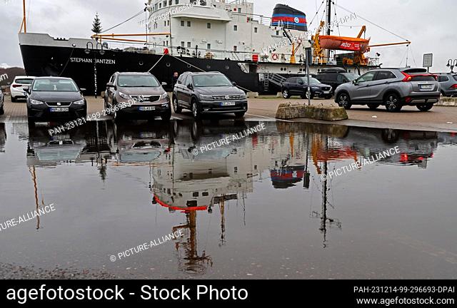 14 December 2023, Mecklenburg-Western Pomerania, Rostock: Cars and the icebreaker ""Stephan Jantzen"" are reflected in a large puddle in the city harbor