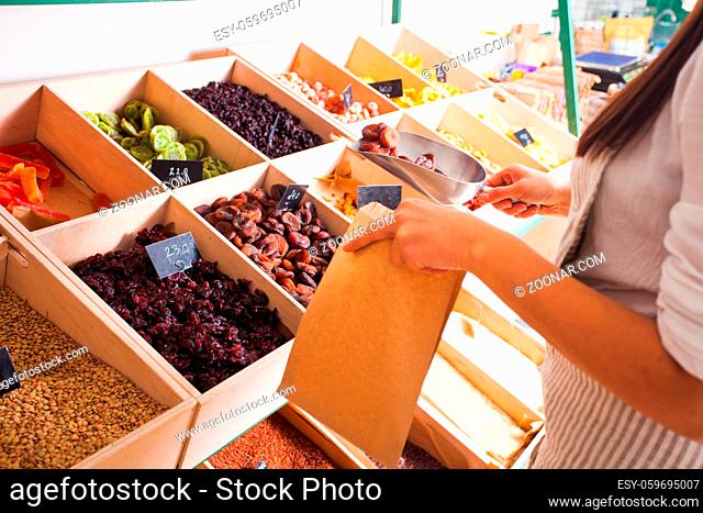 Young woman seller packs dried fruits in a paper bag in the grocery shop