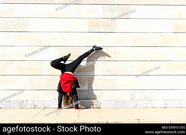 Teenage girl doing a handstand at a wall outdoors