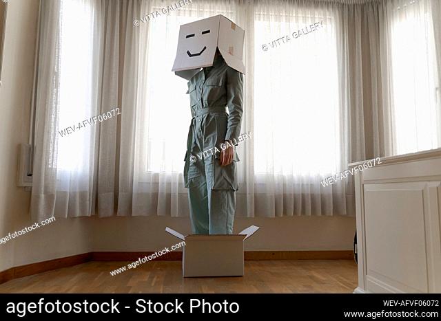 Woman wearing a cardbox on head with bored smiley and standing in box