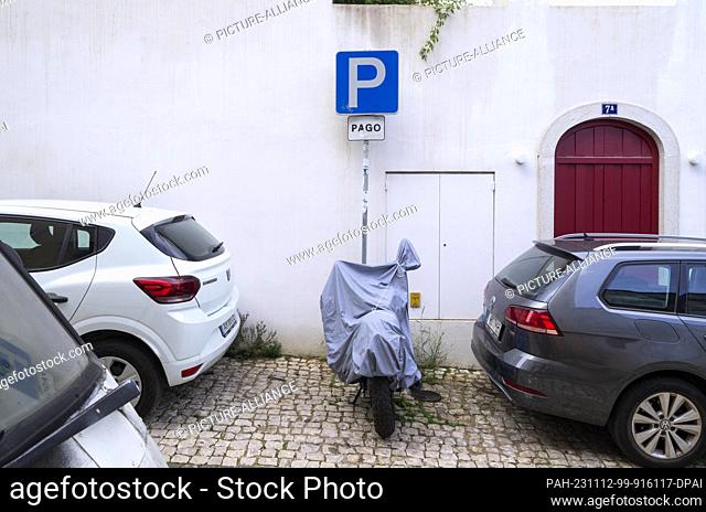 PRODUCTION - 27 October 2023, Portugal, Lissabon: In an alley in the Alfama district, a covered scooter is parked between two cars in front of a parking sign