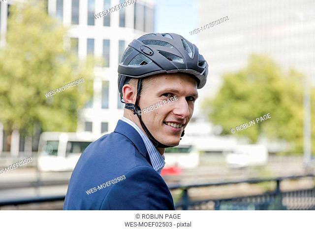 Portrait of smiling young businessman wearing cycling helmet in the city