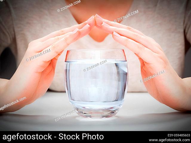 A glass of clean mineral water covered by woman#39;s hands. Concept of environment protection, healthy drink