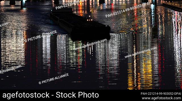 14 December 2022, Hessen, Frankfurt/Main: A cargo ship splits the water of the Main, while the colorful lights of the skyscrapers are reflected in stripes in...